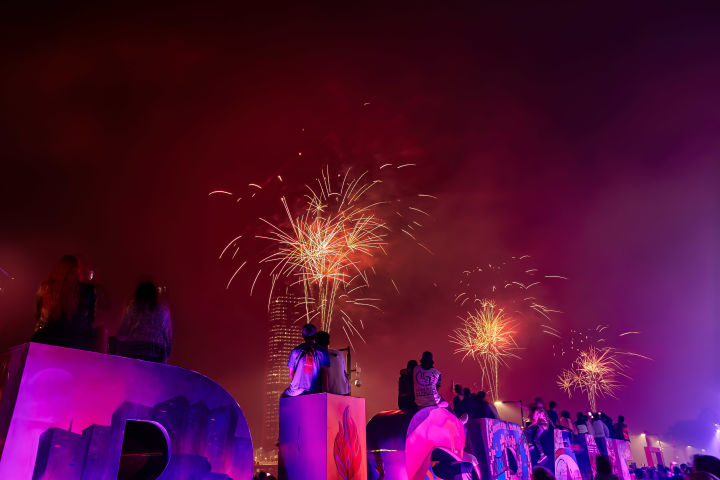 People sitting on gigantic letters spelling "BRISBANE" watching fireworks in the night sky. 